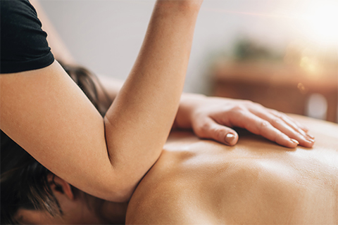A massage therapist uses their elbow on a prone client's back.