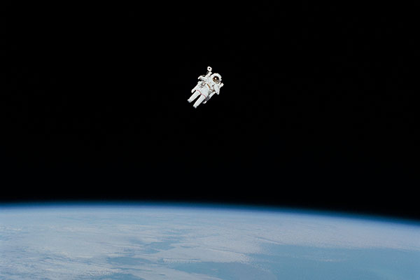 An astronaut floats in space over Earth.